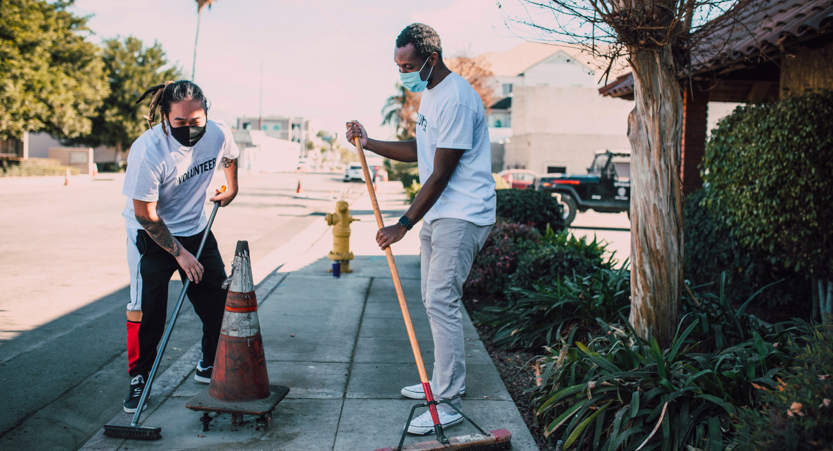 Two men volunteering to clean sidewalk near building
